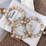 Pistachio, cream, and caramel rounded-cube Bodhi bracelets arranged on soft fabric.