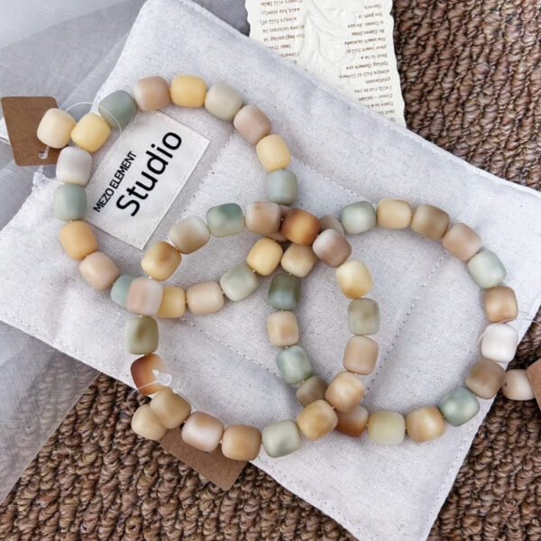 Pistachio, cream, and caramel rounded-cube Bodhi bracelets arranged on soft fabric.