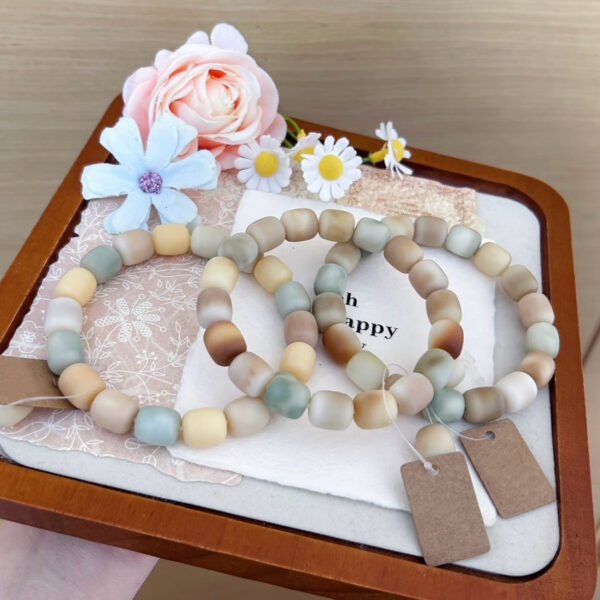 Pistachio, cream, and caramel rounded-cube Bodhi bracelets styled together on a floral display tray.
