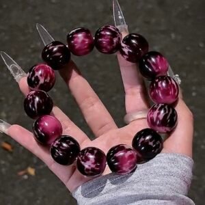Midnight Berry 22mm Bodhi bracelet with glossy deep berry-purple and midnight-black patterned beads held in one hand
