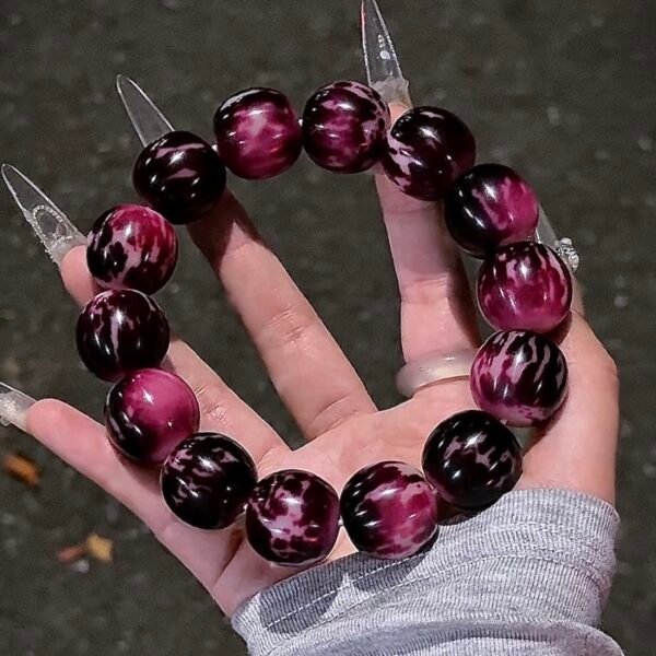 Midnight Berry 22mm Bodhi bracelet with glossy deep berry-purple and midnight-black patterned beads held in one hand